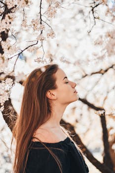 A serene portrait of a woman with long hair amidst blooming cherry blossoms in the park.