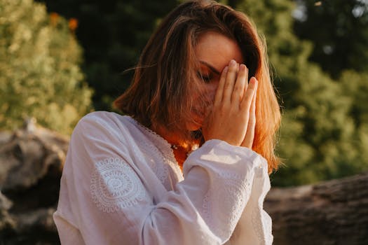 Woman meditating outdoors, eyes closed in peaceful prayer pose.